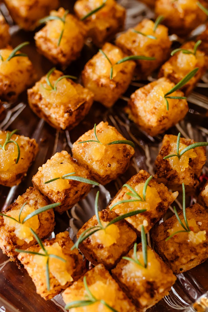 Golden brown tofu cubes garnished with rosemary, perfect for vegan party appetizers.
